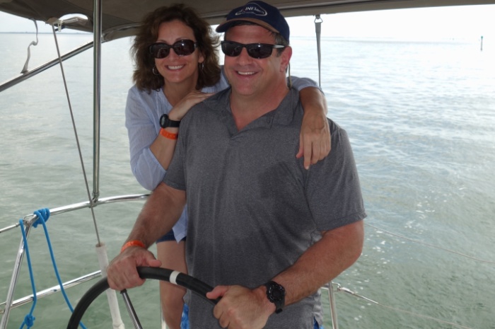 man and woman smiling behind wheel of a sailboat