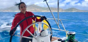 Woman in red jacket with wind in her hair, steering a monohull cruising boat in the British Virgin Islands