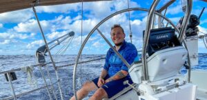 Steve Dirksen with big smile sitting behind the big wheel of an Offshore Sailing School 48' monohull he learned to cruise on