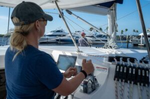 A woman in Offshore Sailing School Fast Track to Boat Handling & Docking course at helm of 40' catamaran entering a marina.