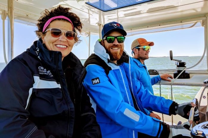 Woman instructor with two men in catamaran cockpit
