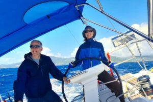 Man standing to left of woman steering a big boat