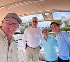 Three guys and a woman in cockpit of sailboat, taking selfie